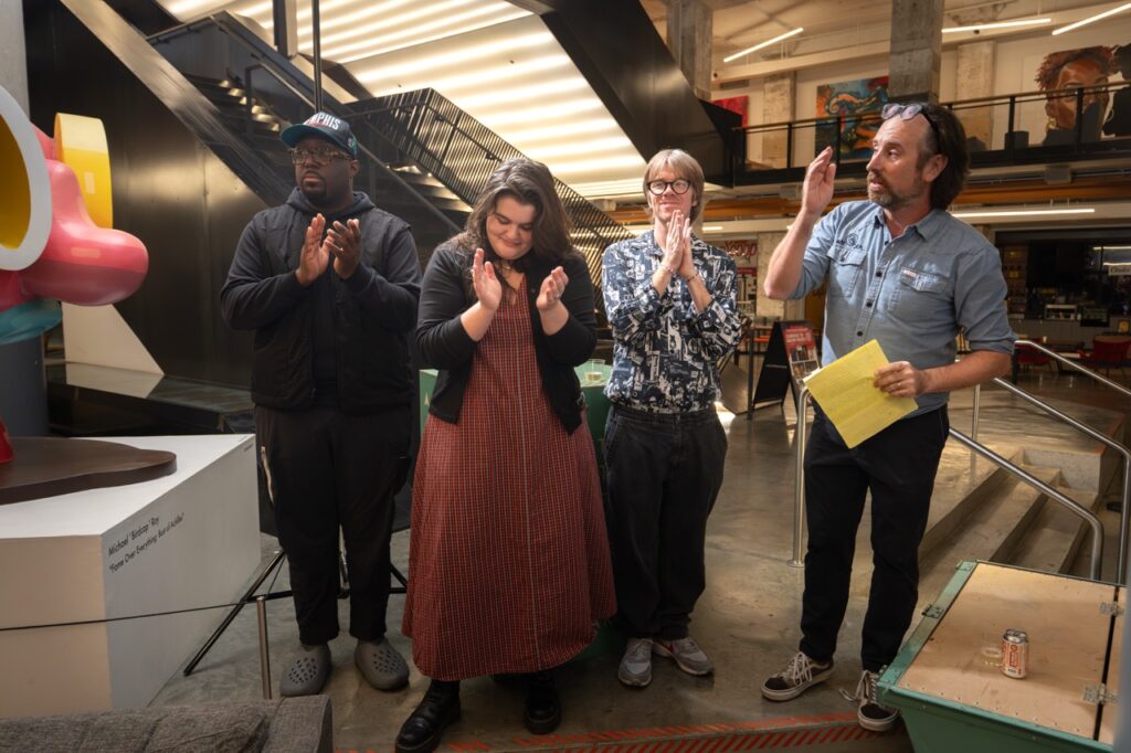 Speakers applaud as a man holding a yellow sheet of paper looks on.