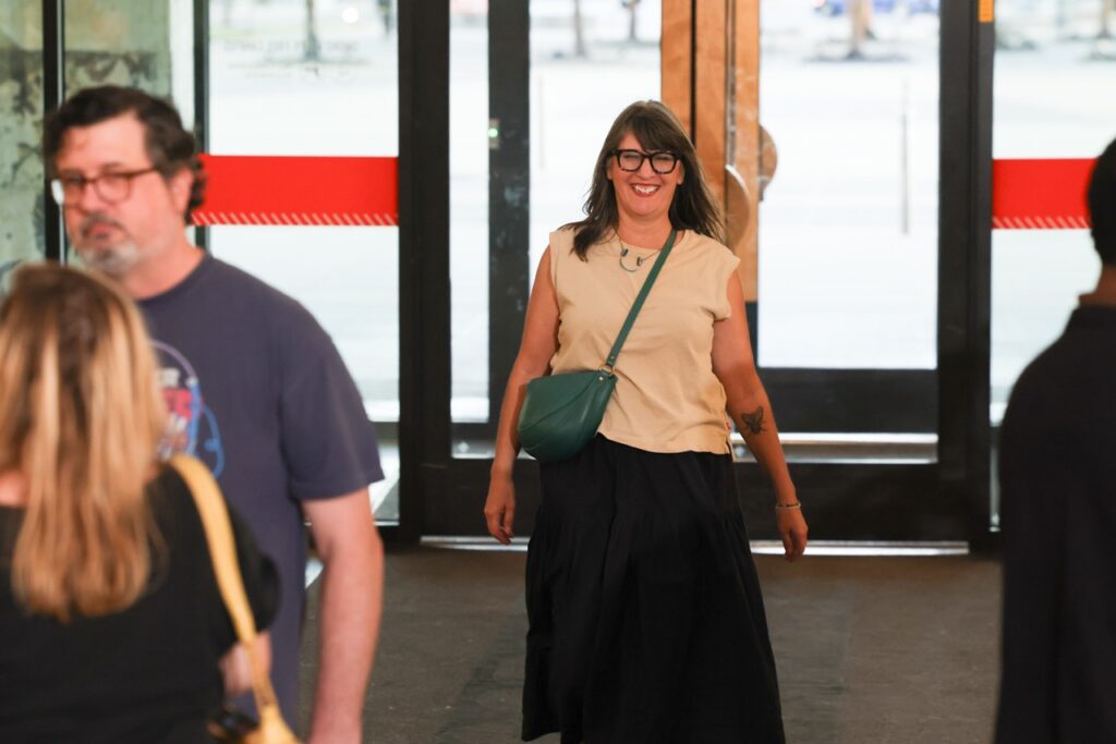 A smiling woman in a cream top walks in through the glass doors while guests look on.