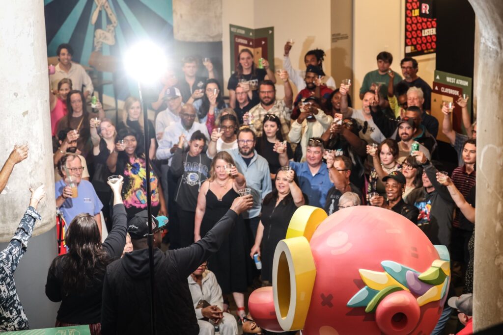 High-angle view of the crowd raising cups in a toast beside a big pink sculpture.