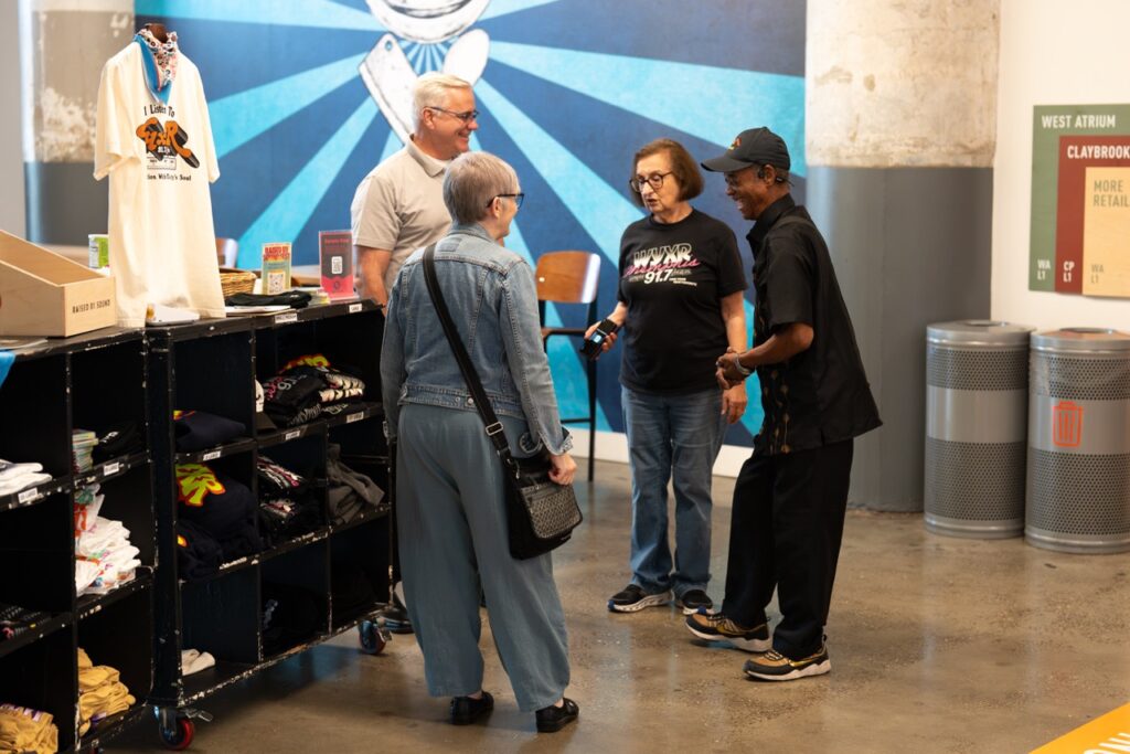 Guests chat beside a rack of WYXR merchandise and T-shirts in the atrium.