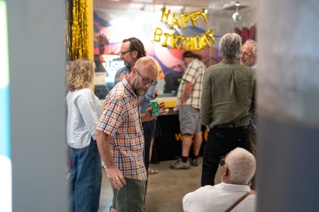 Guests mingle near the studio window with its gold HAPPY BIRTHDAY balloons.