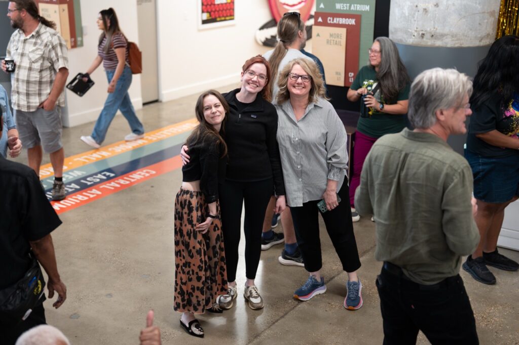 Two women pose arm in arm for a photo while other guests chat around them.