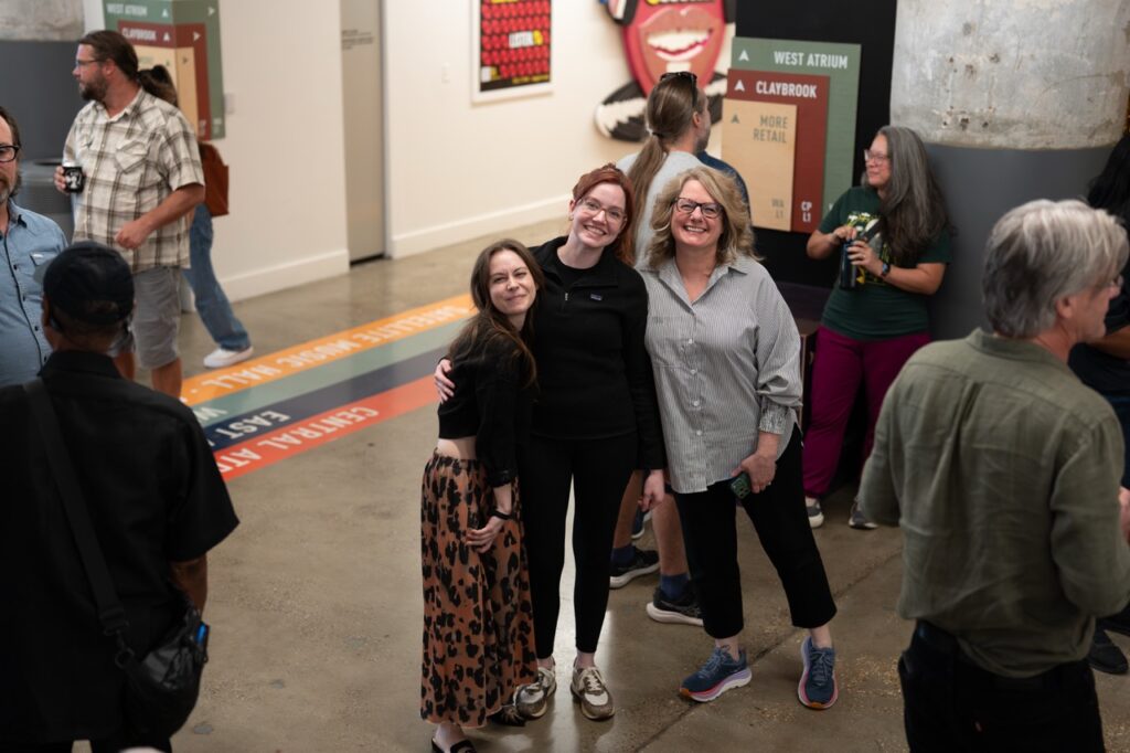 Two women pose arm in arm for a photo while other guests chat around them.