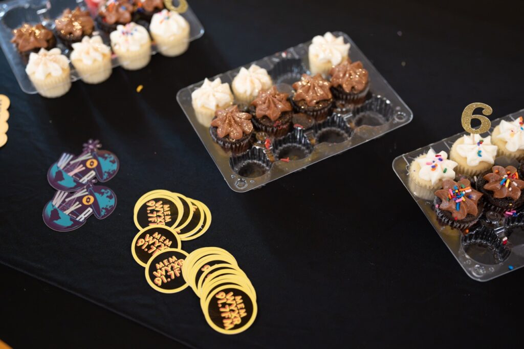Cupcakes in trays sit on a black table with WYXR stickers and gold coin-style buttons.