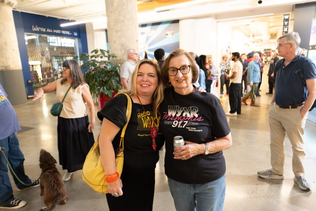 Two women in WYXR T-shirts pose together in the atrium, holding a can and smiling.