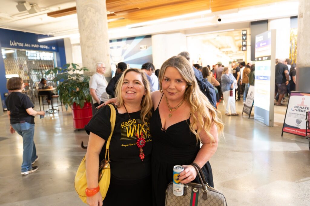 Two women pose together in the atrium as guests mill around behind them.