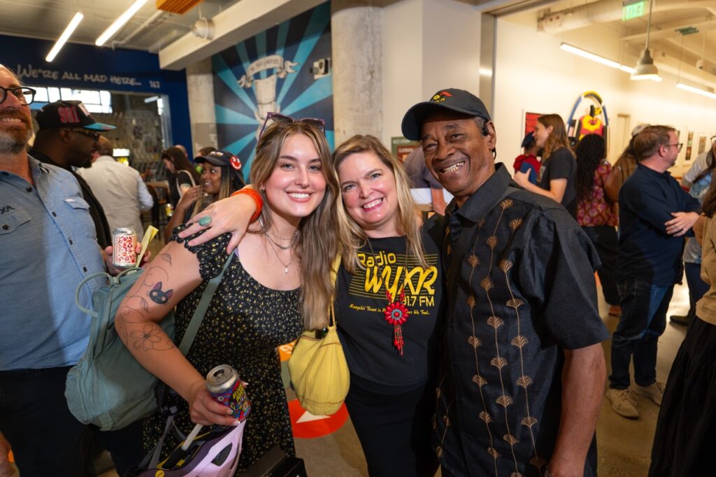 Three friends pose with their arms around each other, smiling and laughing.