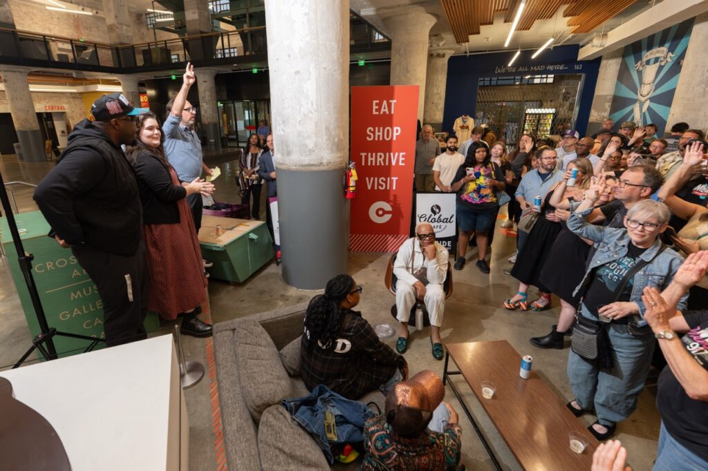 People speak at the front of the crowd while guests look on from the atrium.